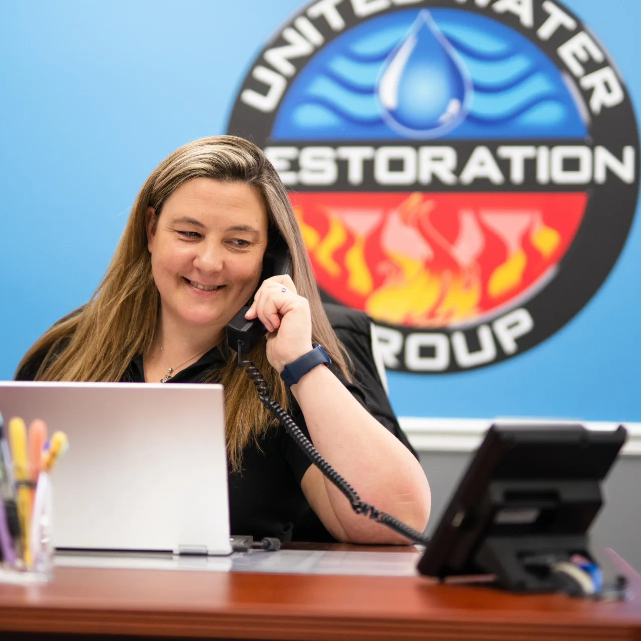 A United Water Restoration Group team member taking a call at the office in front of the company logo